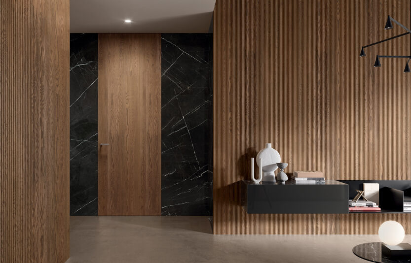 BOISERIE_Comp Porta battente Filomuro con Segno Onda_Rovere Terra Composizione con Porta a Battente Filomuro e boiserie, pantografatura modello Onda. Essenza Rovere Terra e maniglia Pure Cromo Satinato. Rivestimento parete in Marmo Nero Marquina.